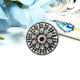 Silver circular brooch with a red gemstone